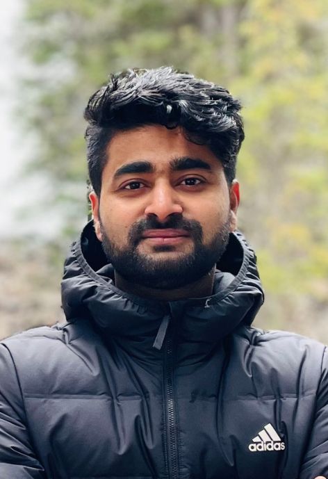 candid photo of suarav pokharel wearing a black adidas brand puffer jacket, taken outdoors with trees in the background