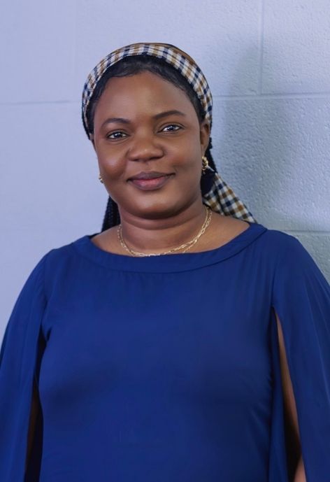 photo of sandra atisey wearing a royal blue blouse and a plaid head scarf in front of a white backdrop.
