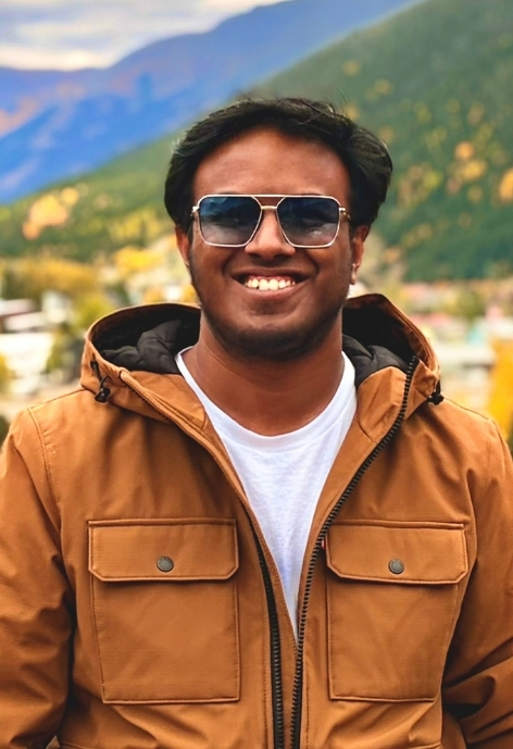 candid photo of rizwan ullah wearing a light brown heavy canvas coat over a white t-shirt, taken out doors with mountains in the background