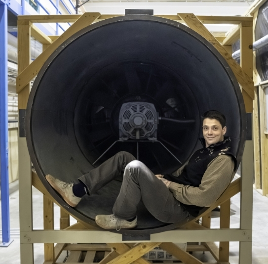Mechanical Engineering student lounging inside the posterior end of the large wind tunnel in the windtunnel laboratory.