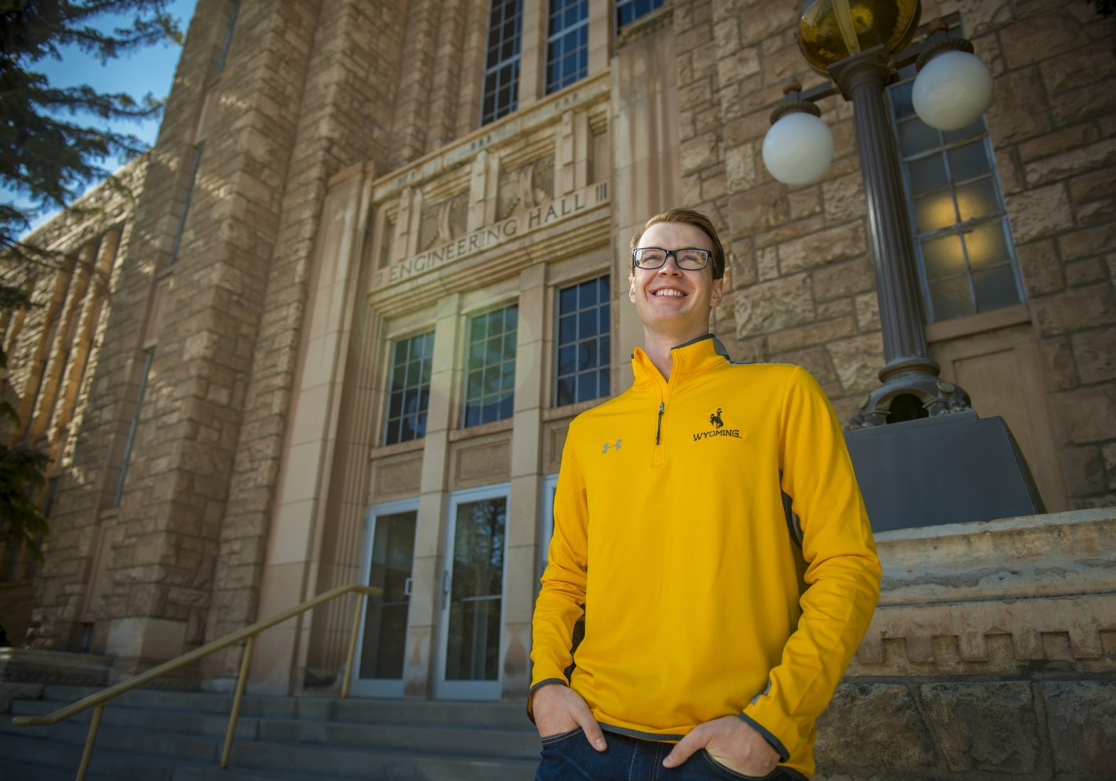 an undergraduate student wearing a UW gold quarter-zip pullover smiles in front of the entrance to the engineering hall.