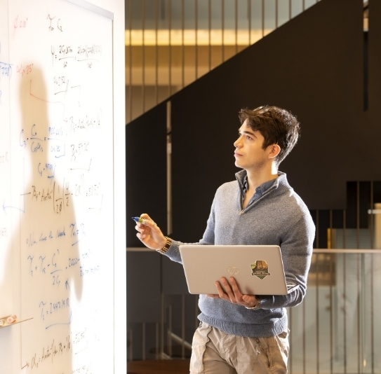 candid photo of an ME student working an equation on a whiteboard in the EERB Collaborative learning space