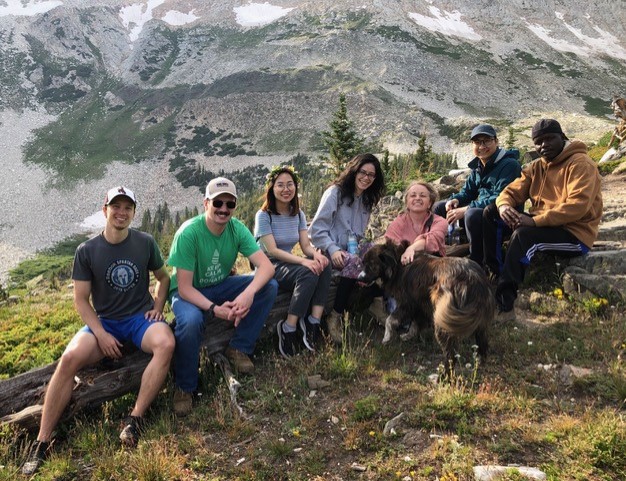 Lab staff sitting on rocks on a grassy landscape in front of the mountain range.