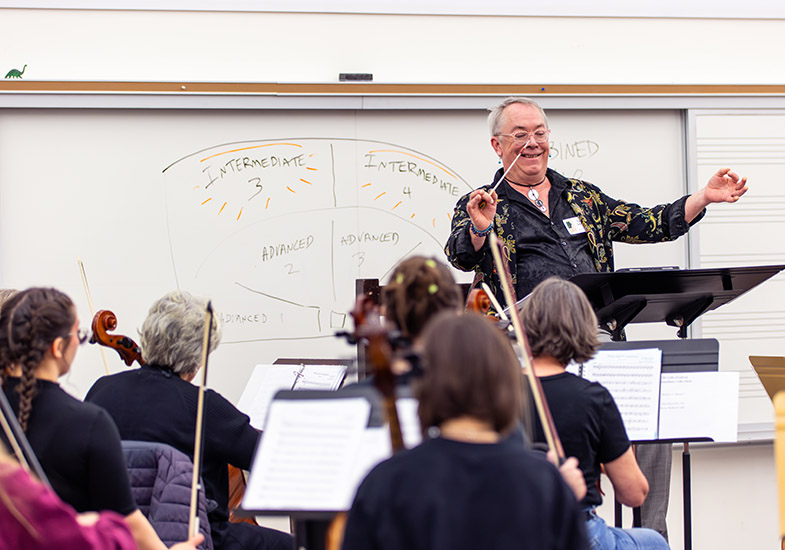 Man conducted in a classroom with students holding string instruments