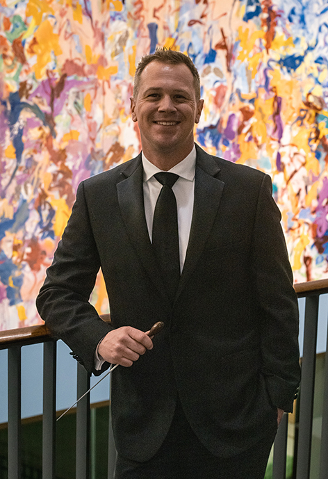 Photo of Dr. Joe Carver smiling in a suit in front of painting inside BCPA
