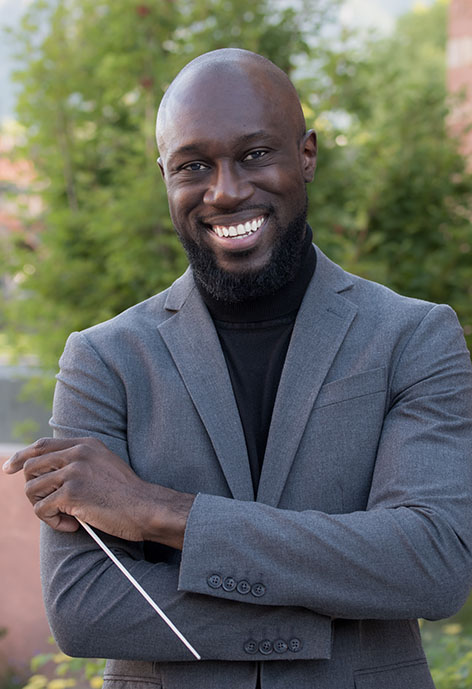 Photo of vocal faculty O'Neil Jones smiling while holding baton