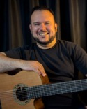 Lecturer Gabriel Santiago holding a guitar while sitting down