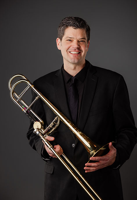 Photo of Dan Watt holding trombone in an all-black suit