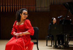 Vocalist in vibrant red dress sitting while singing on stage