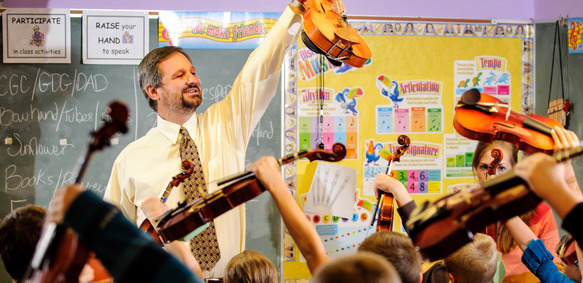 Music teacher and his class hold their instruments up proudly