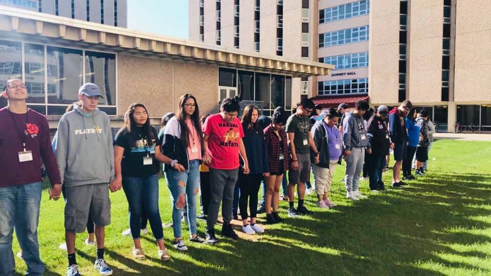 students gather on green field and hold hands