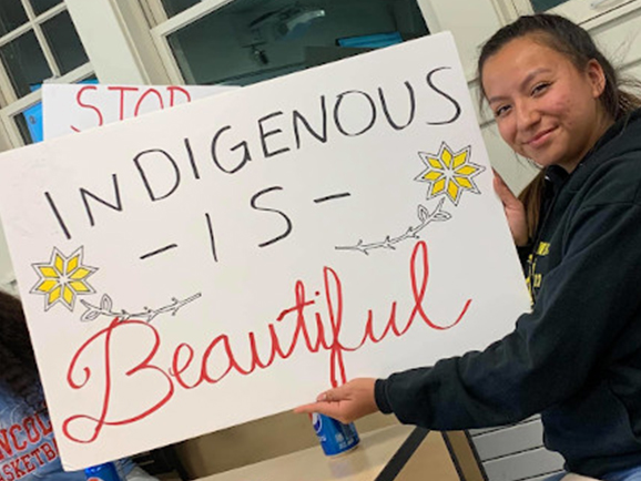 Student holding a sign that says "Indigenous is beautiful"
