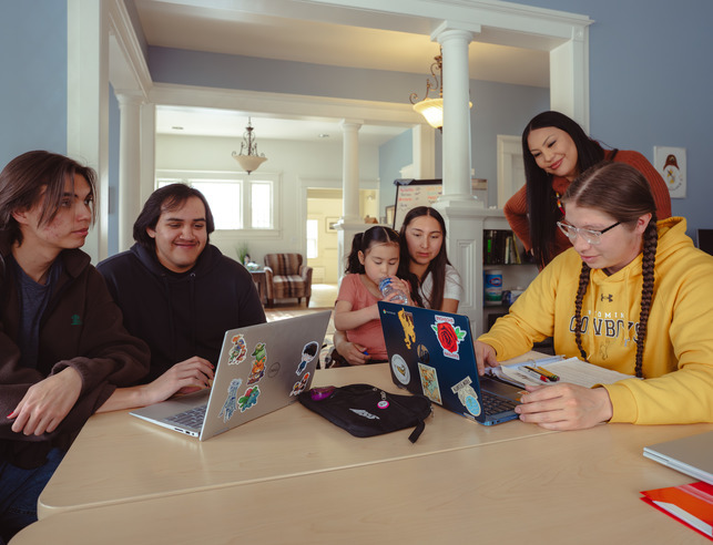 Native American students sitting around a table with laptops, talking, in the NAERCC