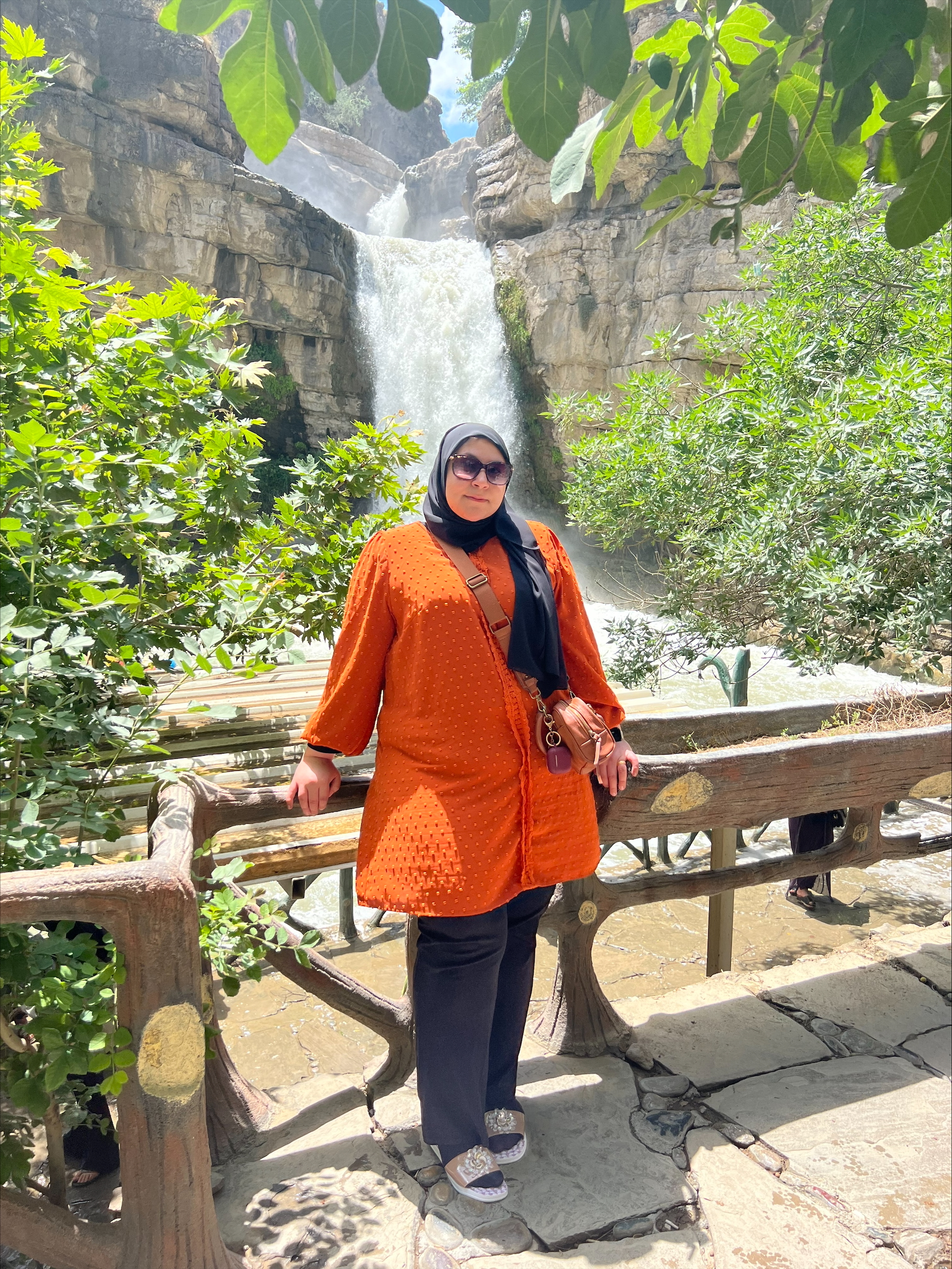 Graduate Student stands by a water fall in an organge coat