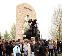 a crowd of people around a statue of a bucking horse and rider breaking through a wall