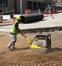 man using soil compacting machine at construction site