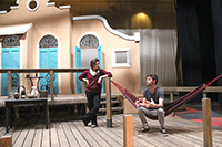 stage set with woman standing and man in hammock talking
