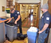 man replacing trash bag in recyling bin while another man stands near