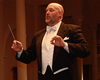 man in white tie and tails with baton raised conducting an orchestra