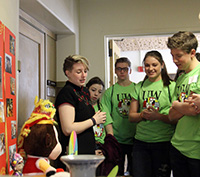 group of students in green t-shirts listening to a woman at a booth
