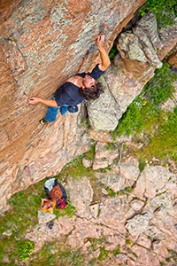 view from above of person climbing rock face with another person on the ground below