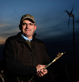 man holding a clipboard with a wind turbine in the background