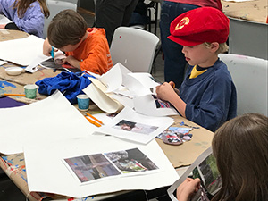 young children working at table with paper, scissors and other art supplies