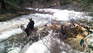 man riding reindeer across rushing stream in snow