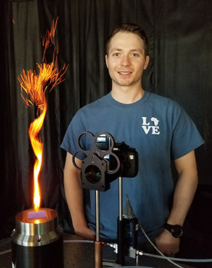 man with lab equipment and a column of fire beside him