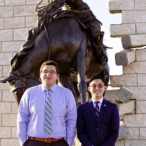 two men standing in front of a statue of a bucking horse and rider