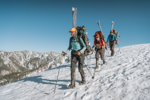 three people with packs and skis hiking on a snowy mountainside