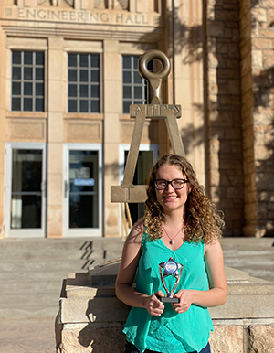 woman holding award in front of sculpture in front of Engineering building