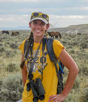 woman standing outdoors with herd of horses behind her