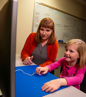 child and adult in front of a computer with child using computer mouse