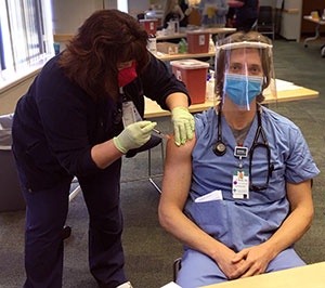 man in scrubs, face mask and face shield getting a vaccine