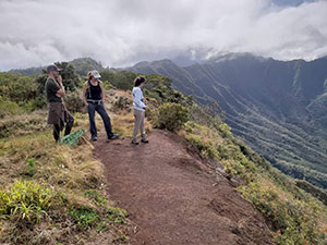 three people on a hill overlooking tropical mountains