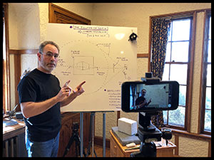 man standing in front of white board in home with phone camera recording him