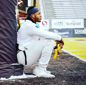 man sitting against padded post and watching field