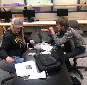 two students working at a table with computers