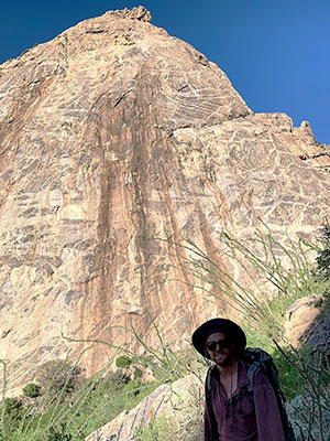 person with tall rock spire behind him