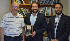 three men standing together with the middle one holding a plaque