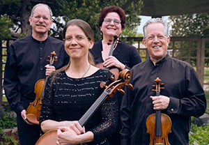 four people posing with string instruments