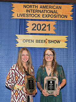 two women holding placques and standing under a sign