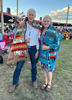 man and woman standing together draped with Native pattern blankets