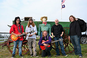 group of people, two with guitars, posing in front of an old wagon