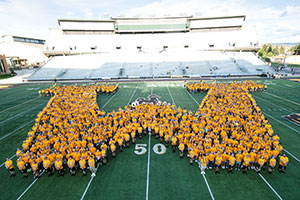 students in yellow shirts filling in an outline of the letter W on the football field
