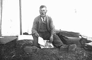 black and white vintage photo of a man sitting on the ground with piles of papers