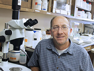 man in a lab beside a large microscope