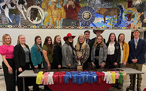 large group of people posing at a table with prize ribbons and a trophy