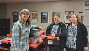 three people posing with red and black plastic boxes